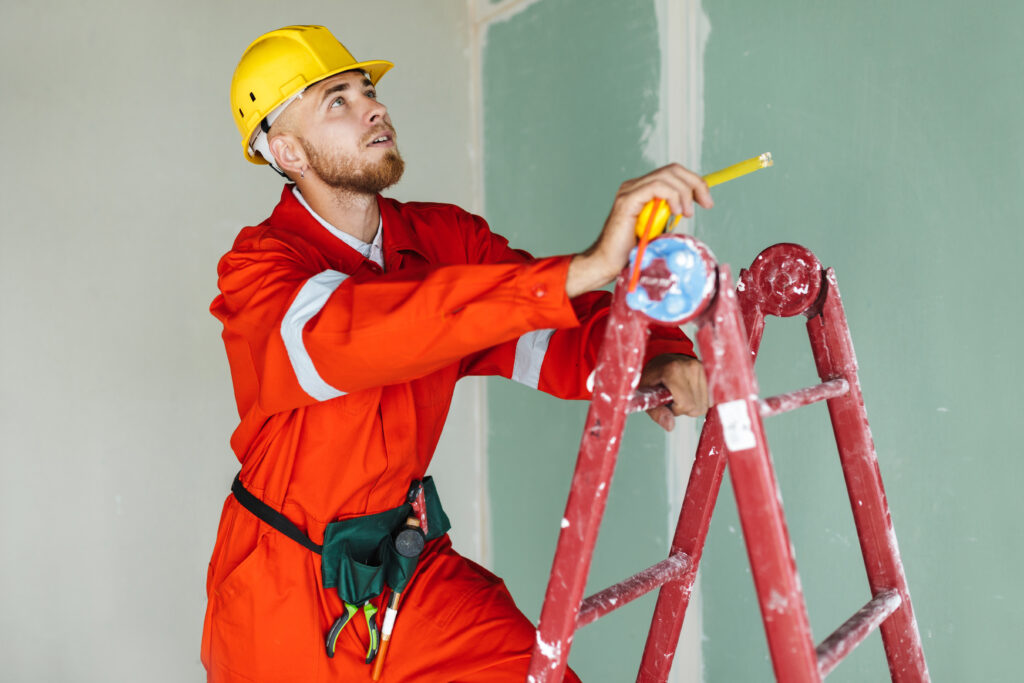 Young builder in orange work clothes and yellow hardhat standing